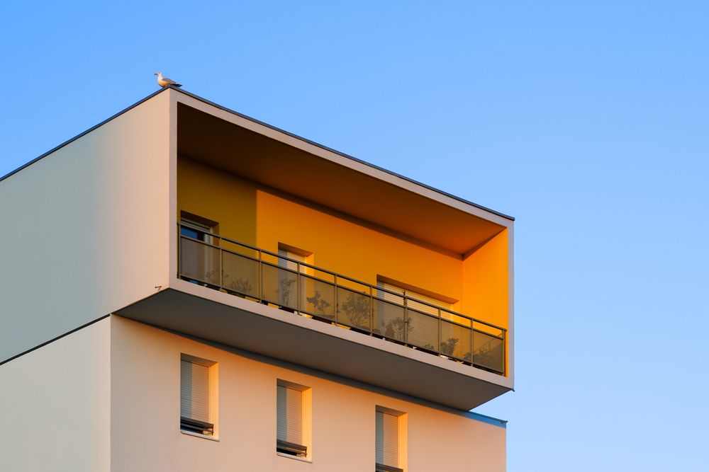 Angle d'un immeuble d'appartements moderne avec un balcon éclairé d'une lumière orangée et une rambarde métallique