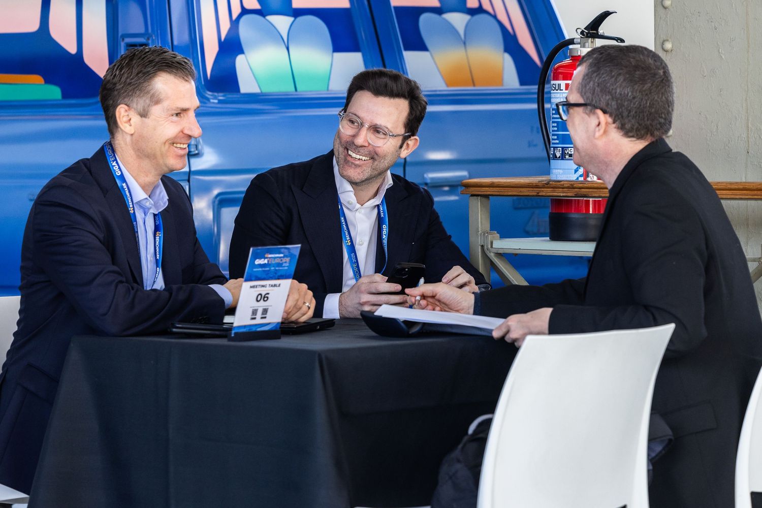 Three business professionals in suits engage in a lively discussion at a round table during a corporate conference event.