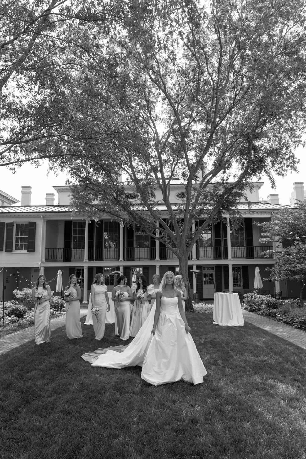 Bride in white ball gown with bridesmaids in yellow dresses on lawn of historic estate.