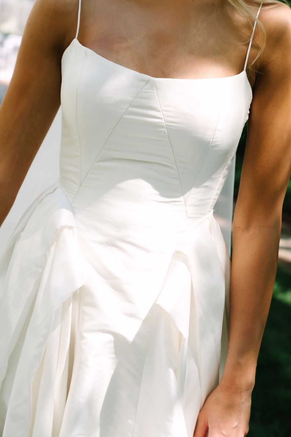 Close-up of bride in elegant white satin corset wedding gown with spaghetti straps.