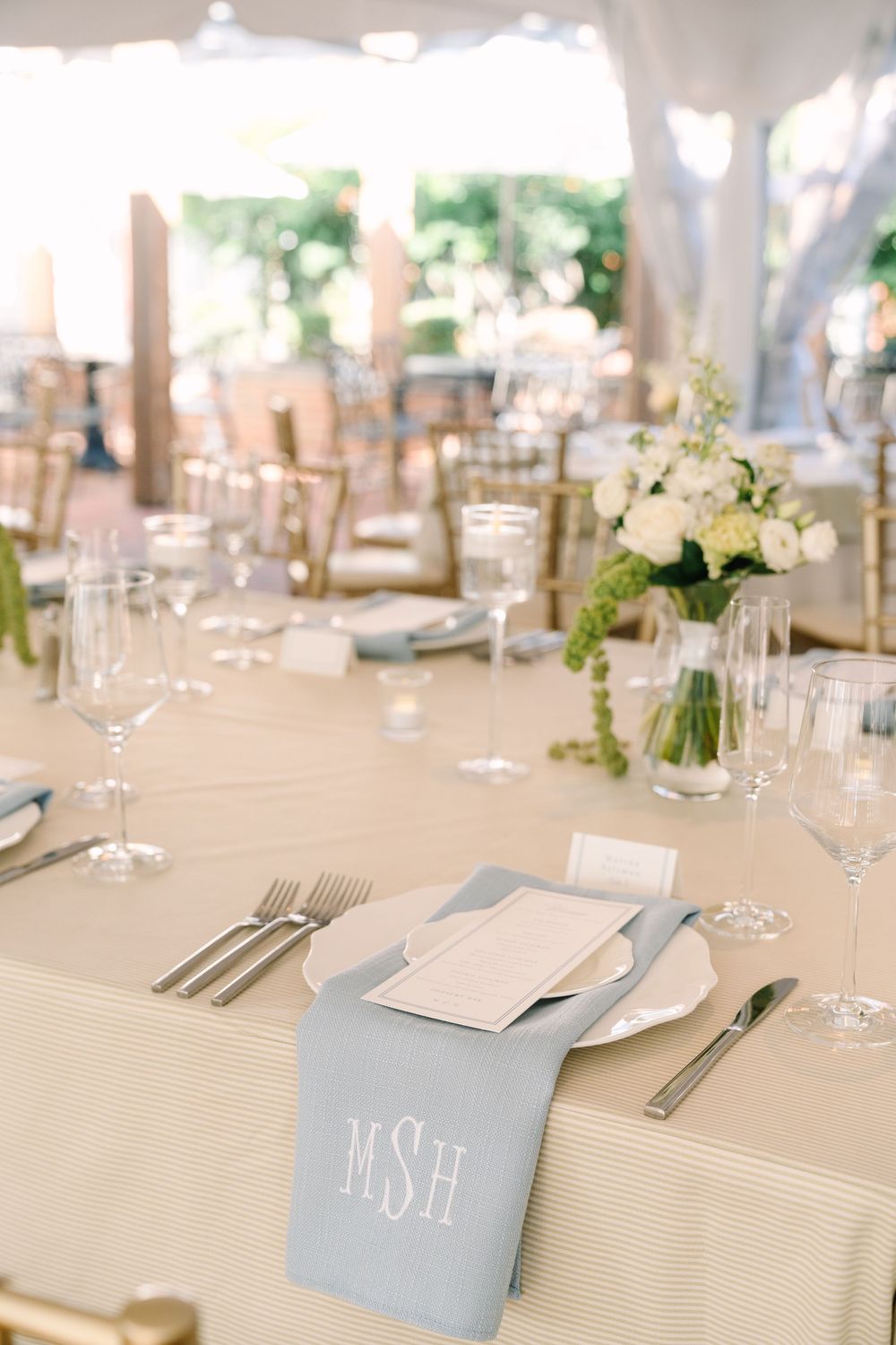 Elegant wedding table setting with blue monogrammed napkin, white florals, and crystal glassware.