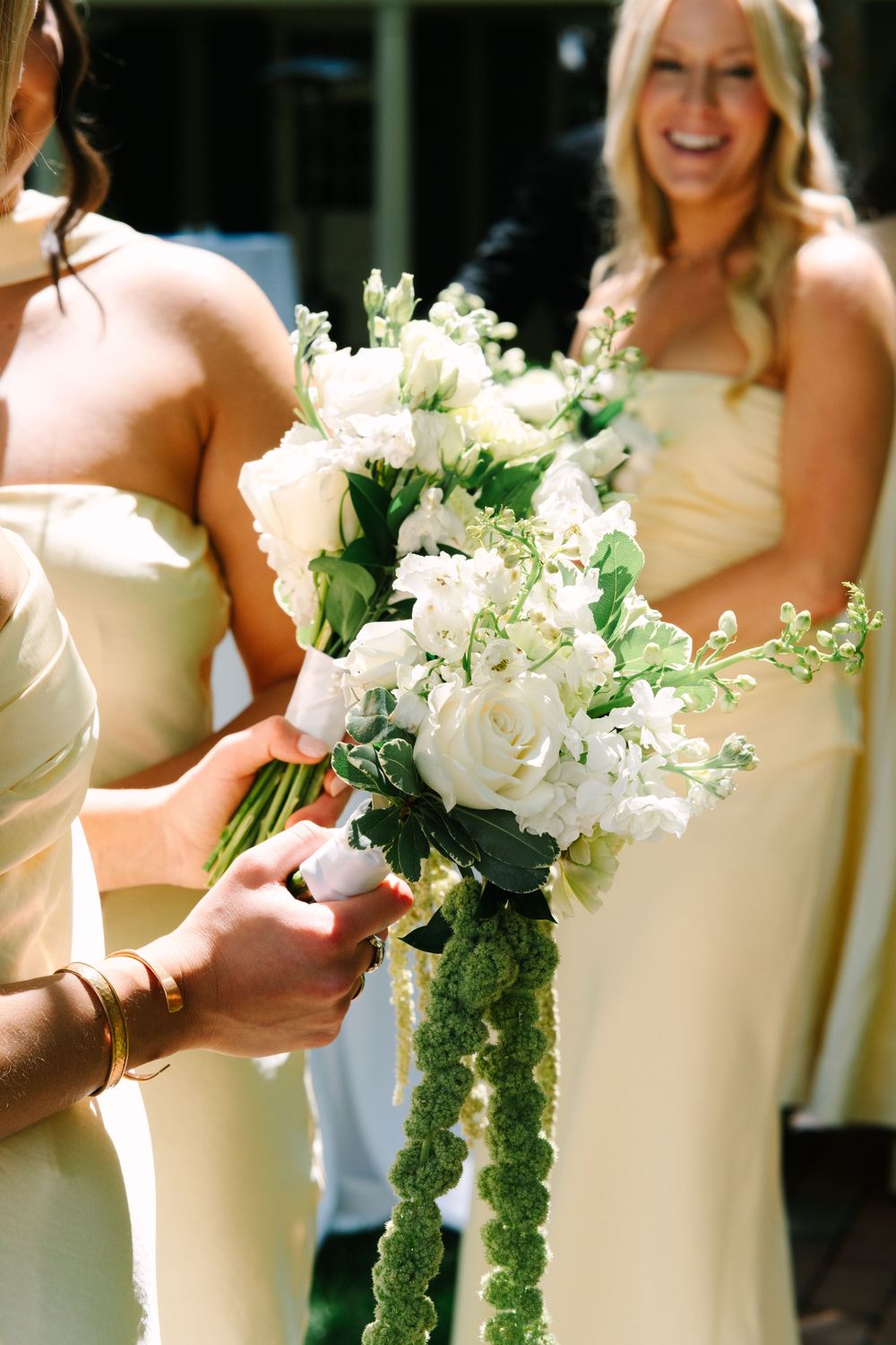 Bridesmaids in yellow dresses holding white rose bouquet with green amaranthus at a wedding.
