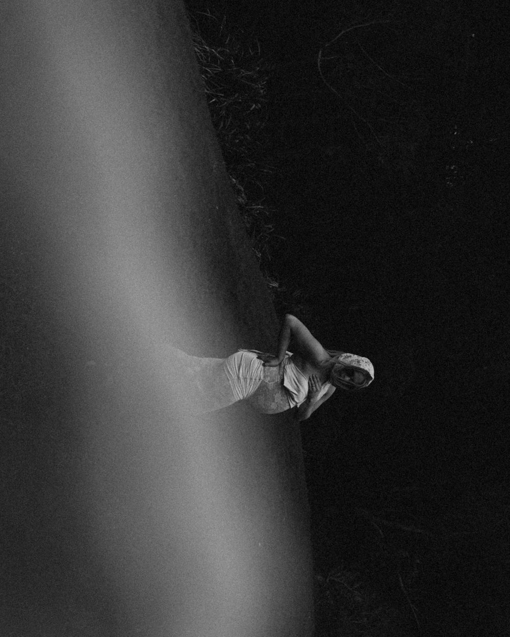 Black and white photo of a person in white dress standing in dramatic light against dark background.