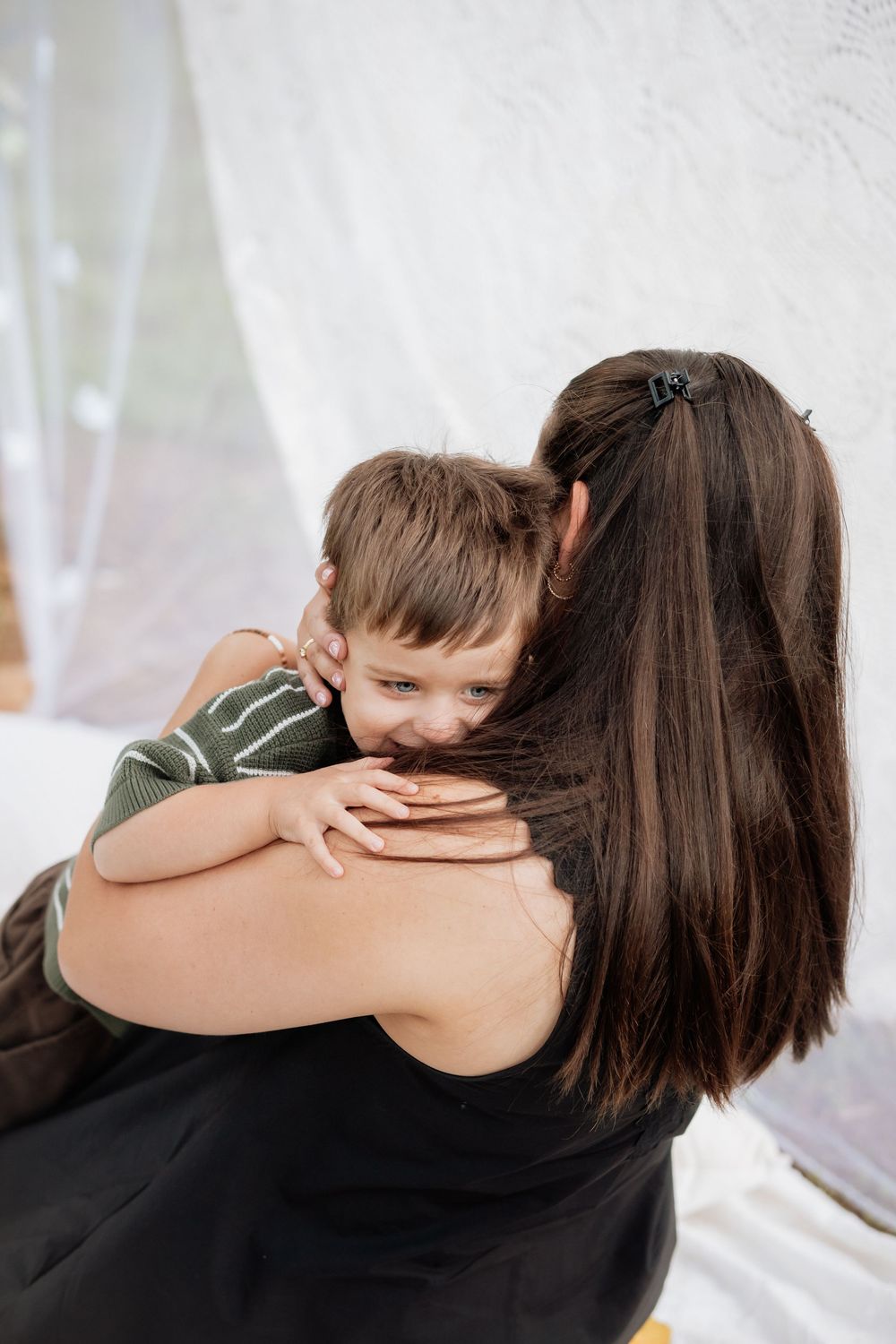 Tender embrace captured against white lace background with child in olive striped shirt.