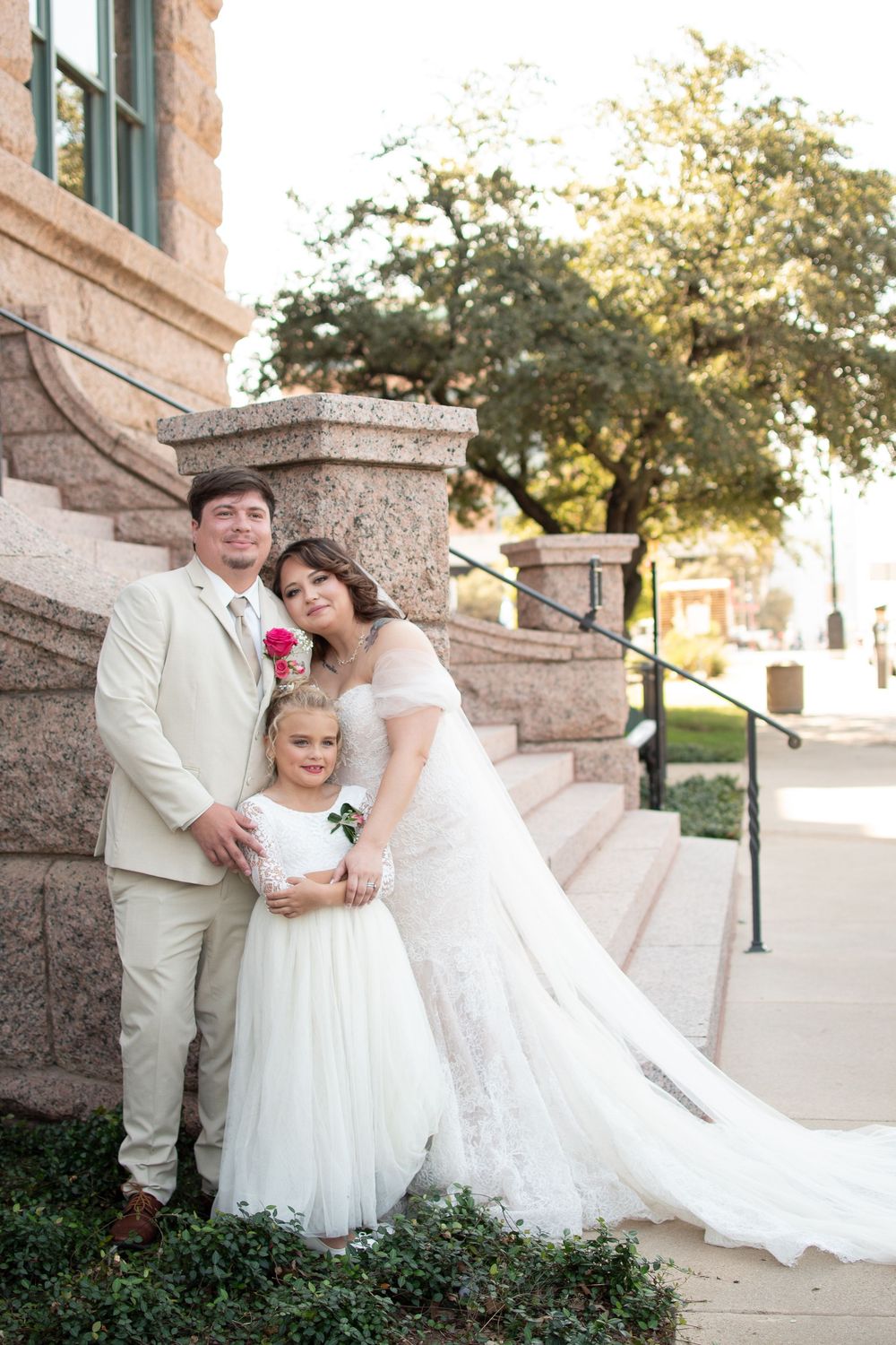 Newlyweds pose with their flower girl on the stone steps outside the Tarrant County Courthouse in downtown Fort Worth.