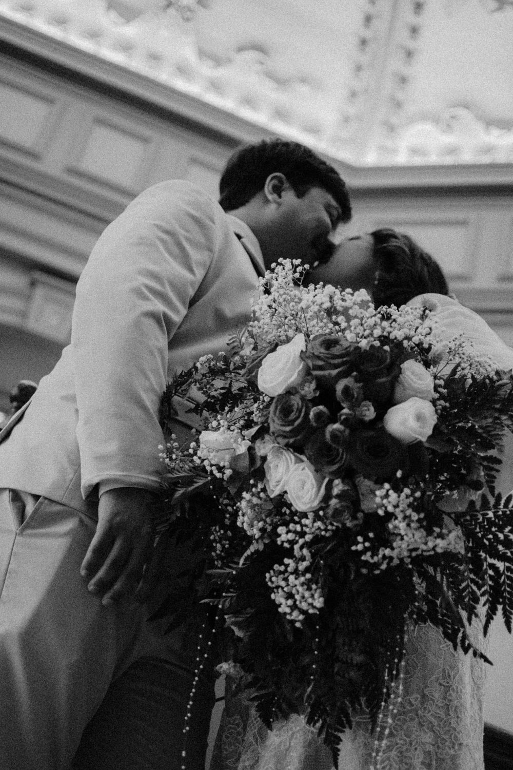 Black-and-white portrait of newlyweds kissing near the Fort Worth courthouse with the bride's red bouquet in the foreground.