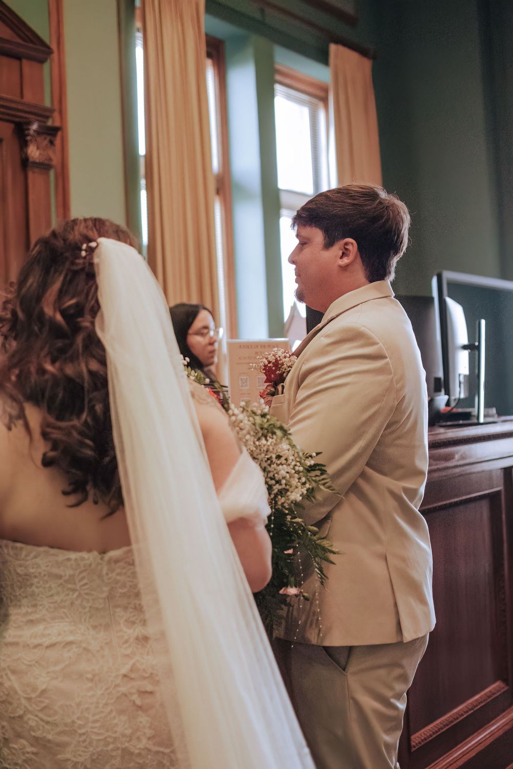 Bride and groom stand together during their Fort Worth courthouse wedding ceremony, she in a lace gown and he in a tan suit.