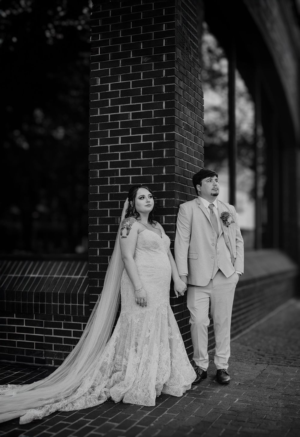 Black-and-white portrait of a bride and groom leaning against a brick wall during their downtown Fort Worth wedding photos.