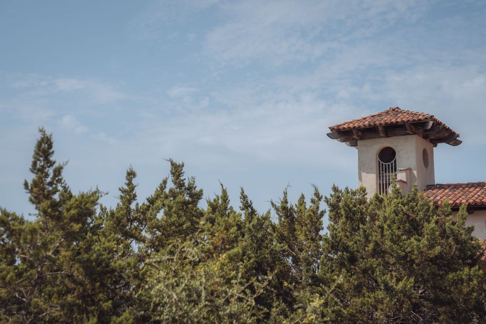A red-tiled tower rises above lush green trees against a partly cloudy blue sky.