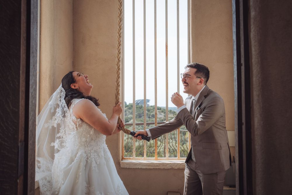 Bride and groom share a joyful first look moment, holding hands by a sunlit window in an elegant venue.