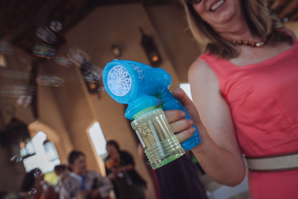 Woman in pink dress holding a blue bubble gun machine at a festive indoor celebration.