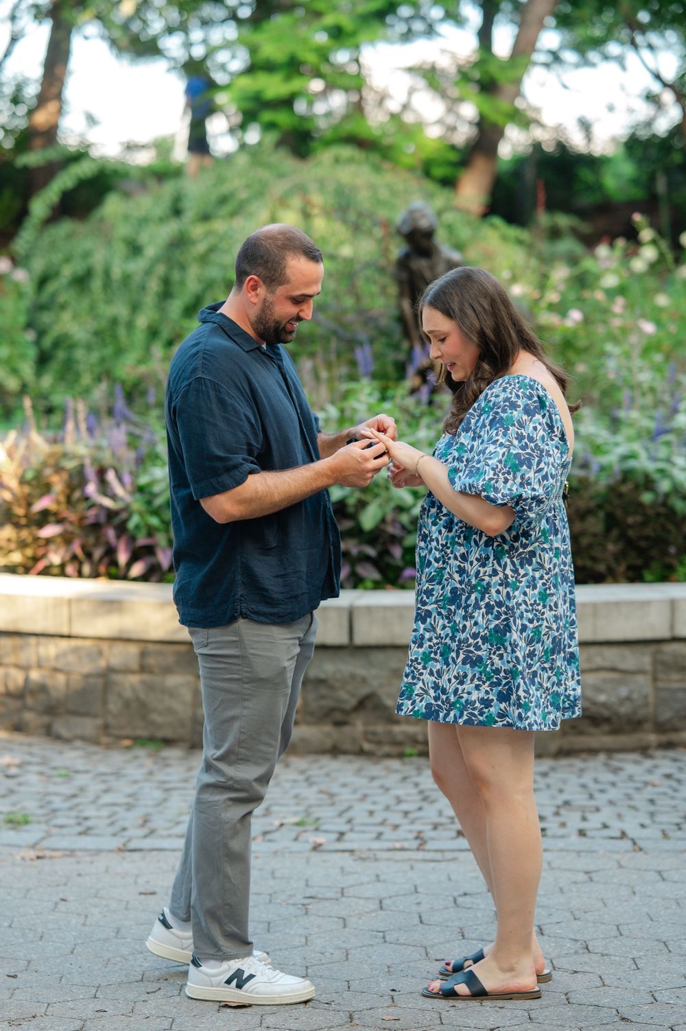 A man places an engagement ring on a woman's finger in a lush garden setting during a romantic proposal.
