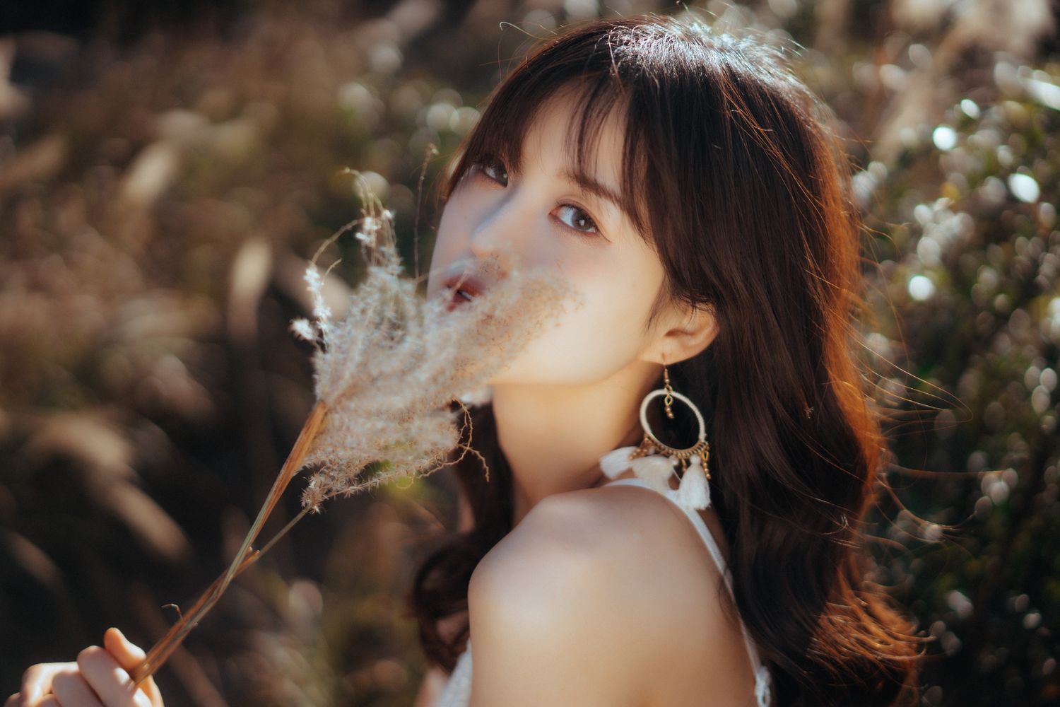 Woman with long dark hair blowing dried flowers in golden sunlight.