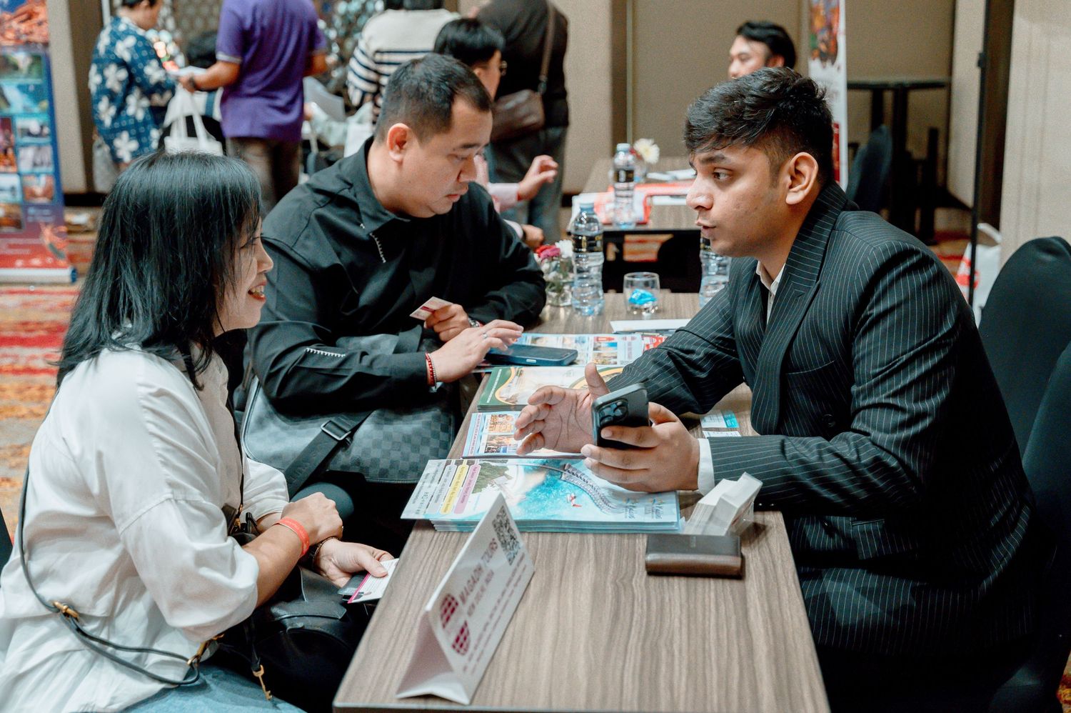 Three professionals in formal attire engage in a business meeting at a table during a corporate networking event.