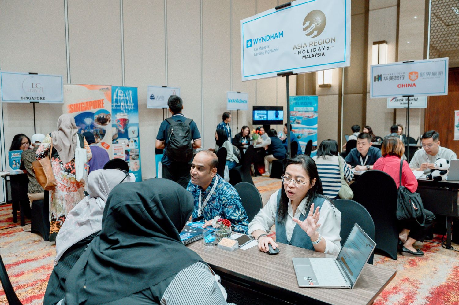 Business professionals networking at a conference expo with Wyndham and other brand booths in the background.