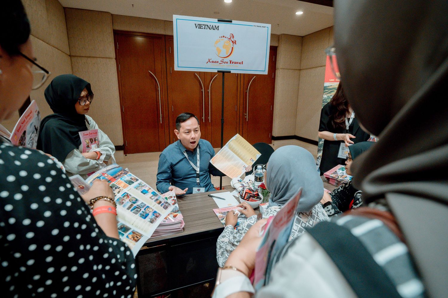 Vietnam tourism representatives meet with travel agents at a business networking event, reviewing brochures at a conference table.