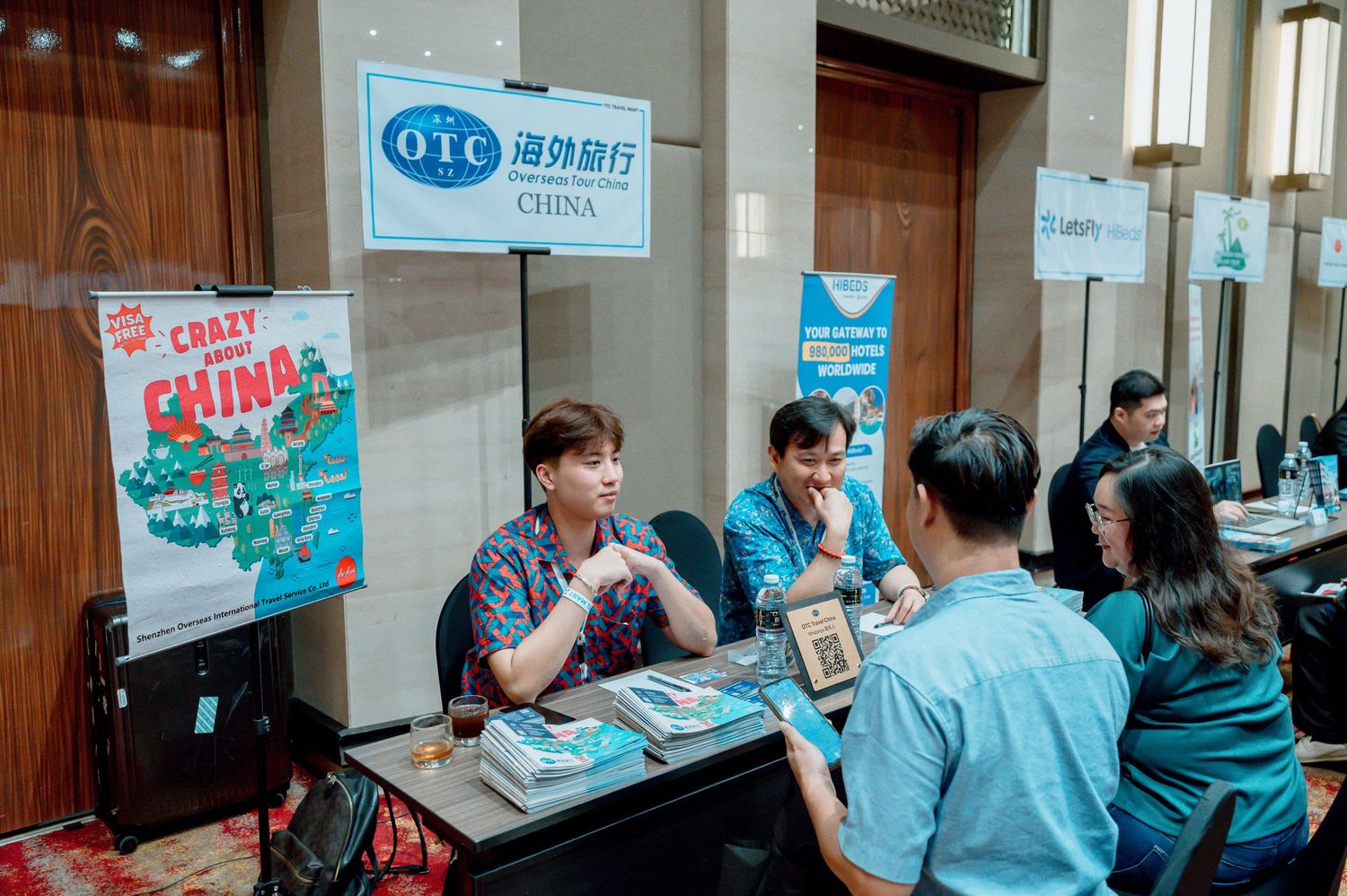 OTC China travel booth with representatives meeting clients at a tourism expo, featuring Crazy About China promotional materials.