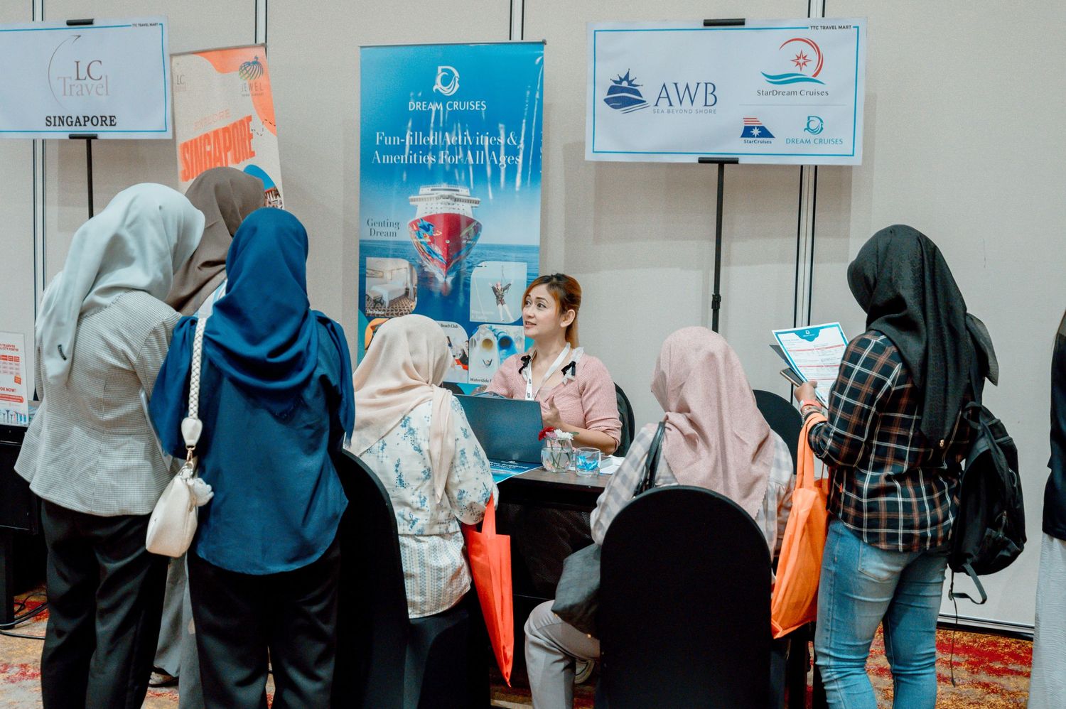 Job fair booth with AWB Singapore banner, recruiter engaging with hijab-wearing candidates at an indoor career event.