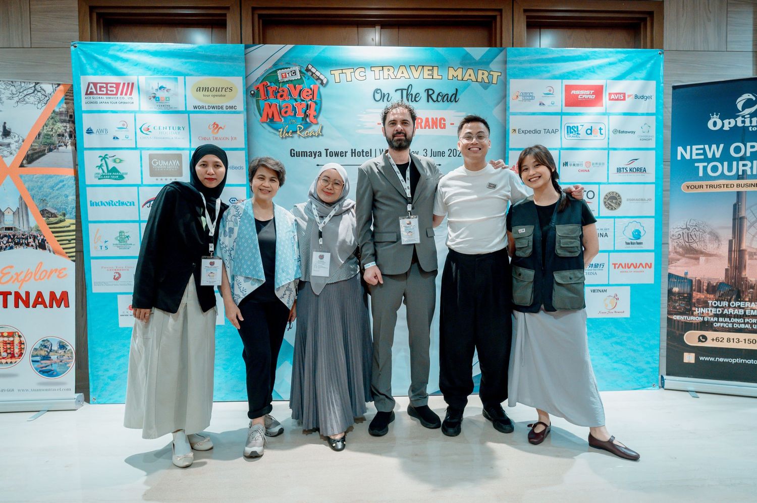 Six people posing together at a travel conference event with promotional banners in the background.