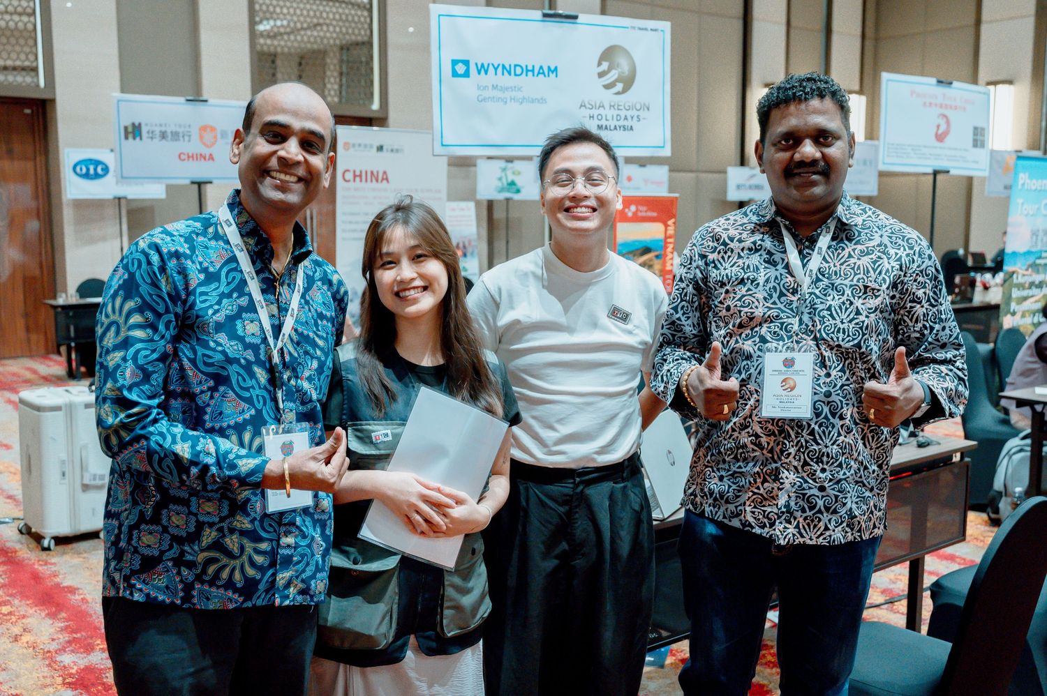 Four professionals smiling together at a Wyndham conference event, wearing batik shirts and lanyards.