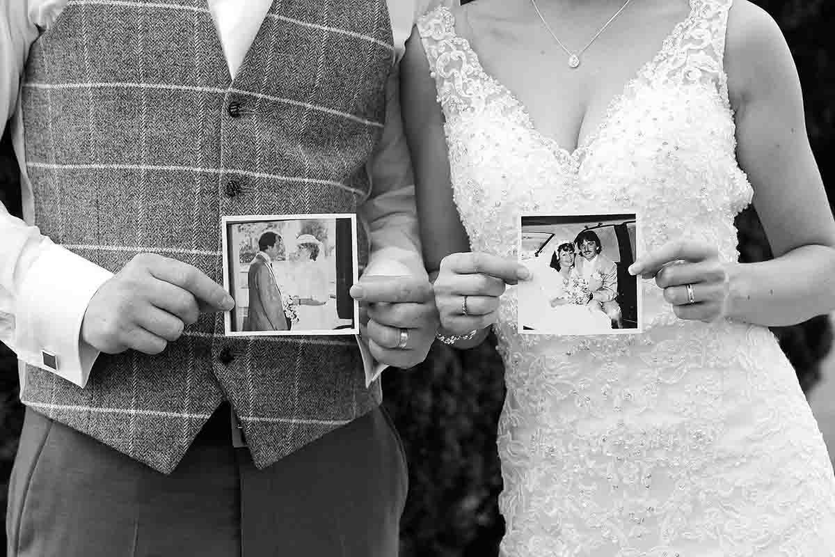 Black and white wedding photo of bride and groom holding vintage photos of their parents on their wedding day.