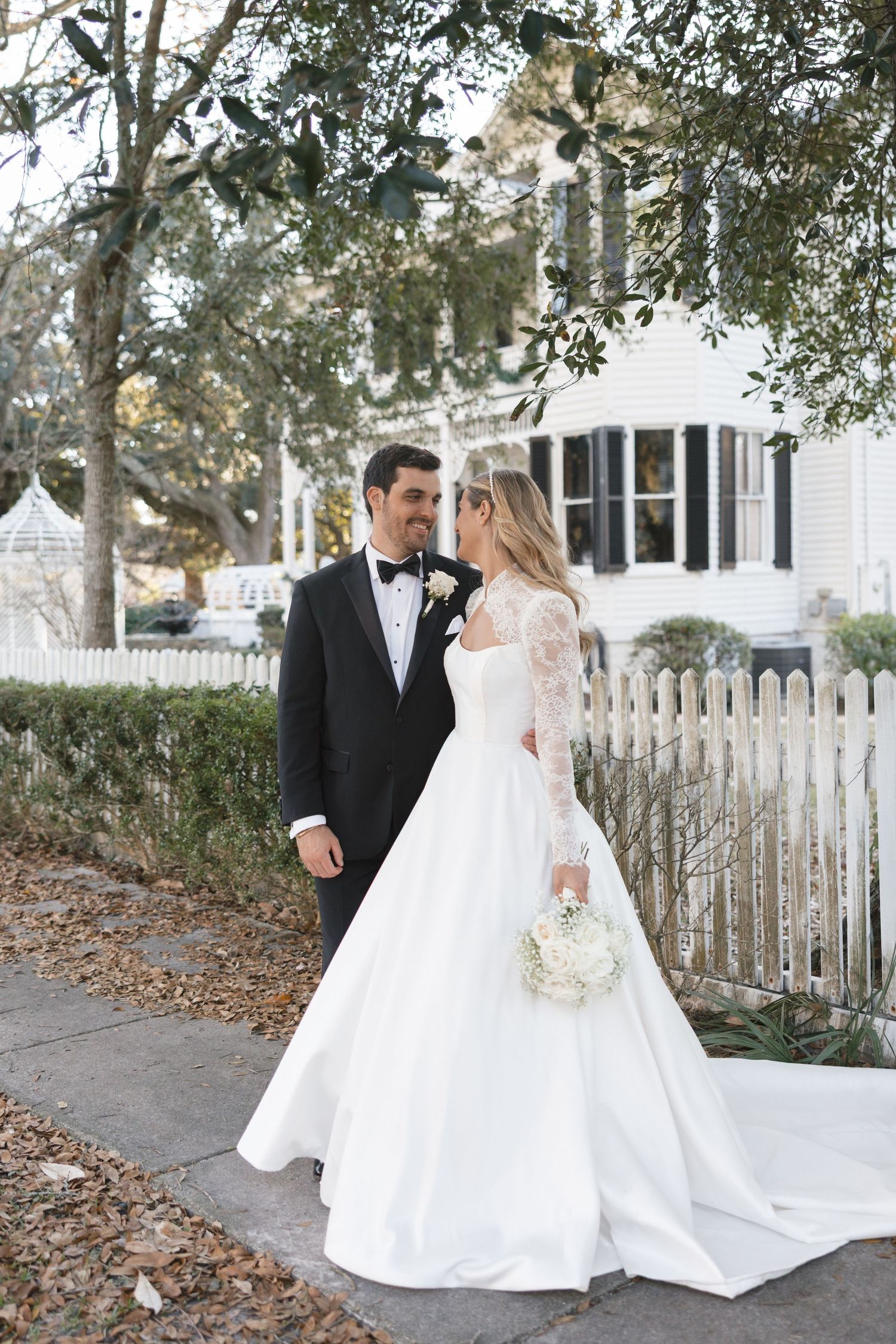 Bride in a lace ball gown and groom in a tuxedo posing on a charming Southern street.