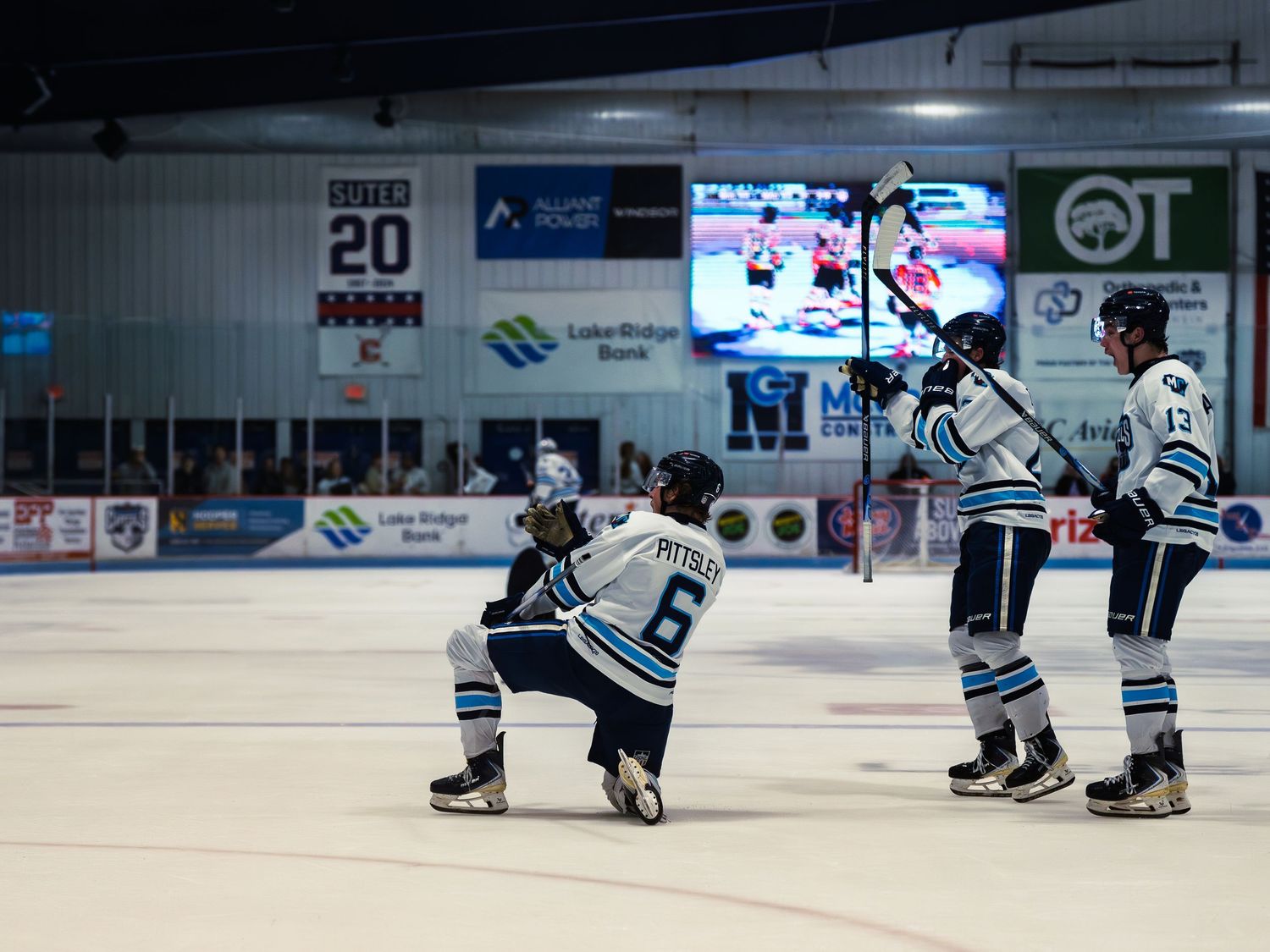 Three Madison Capitols players celebrate a goal, one dropping to a knee with a fist pump while two teammates raise their sticks.