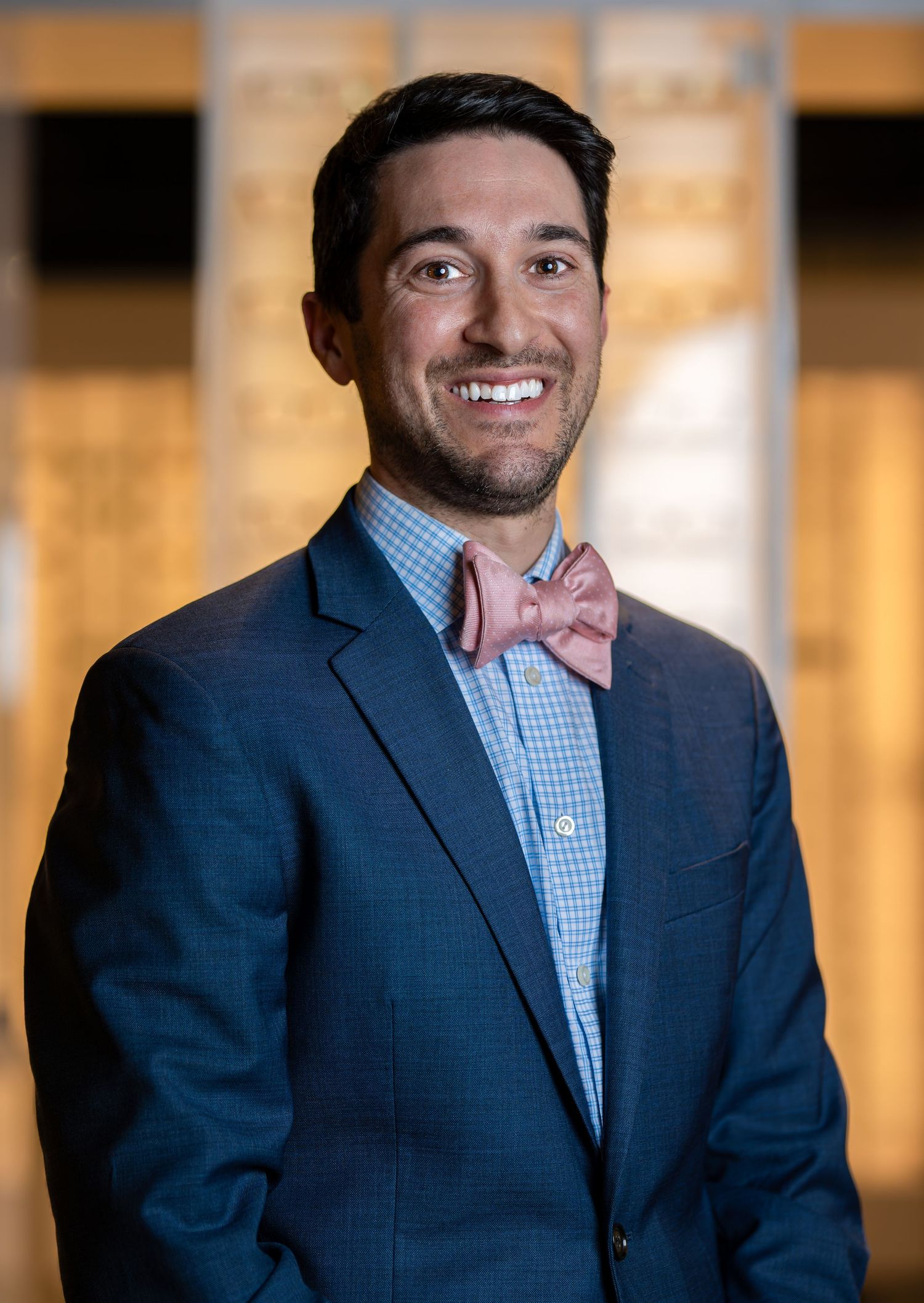 Smiling professional man in navy blazer and pink bow tie posing for corporate headshot portrait.