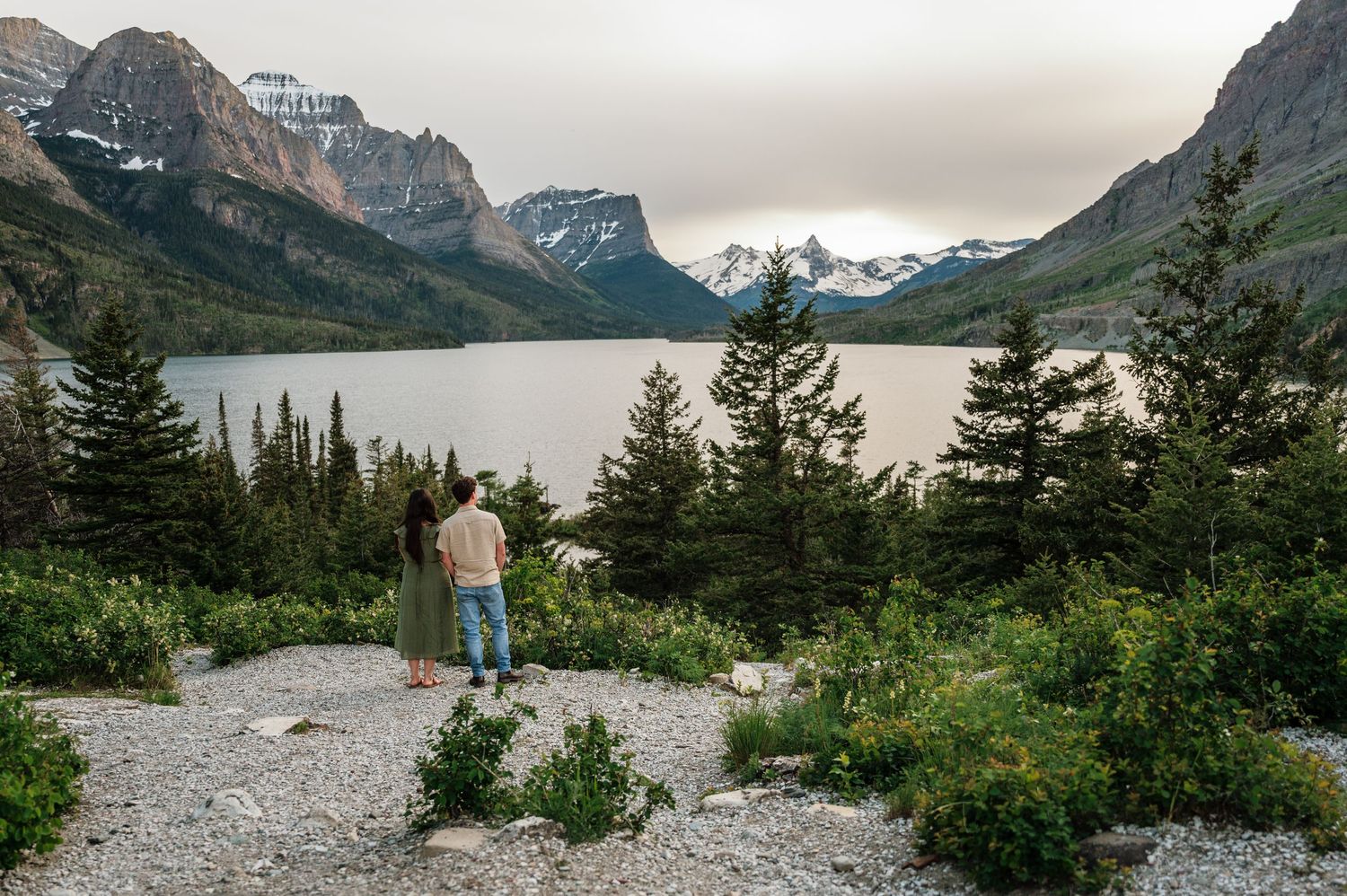 Couple admiring stunning mountain lake views surrounded by pine trees at Glacier National Park.