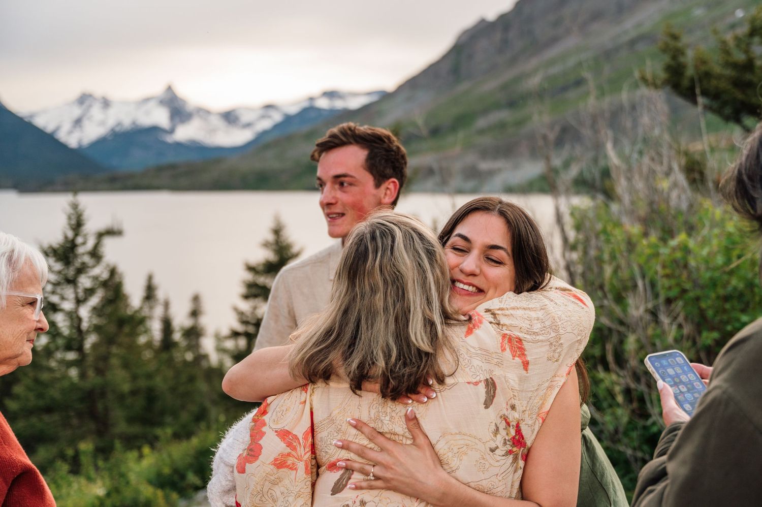 Couple embracing guests at outdoor wedding ceremony with mountain lake backdrop in Glacier National Park.