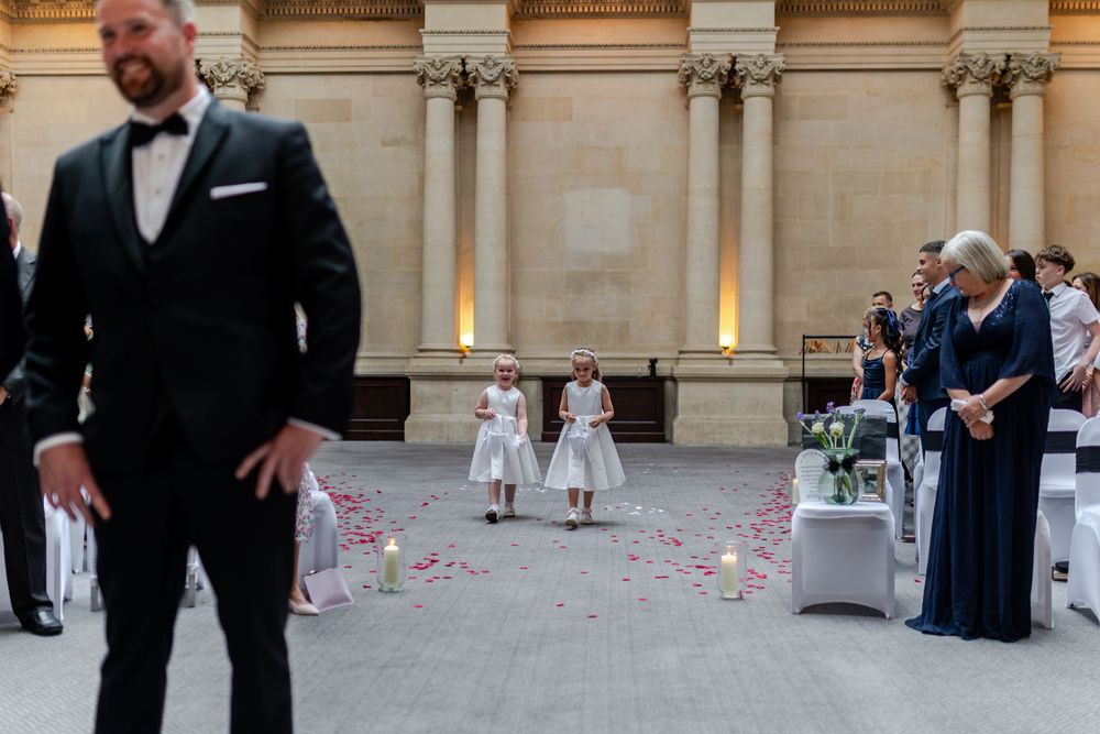 Two flower girls walk down an outdoor wedding aisle lined with candles and rose petals at an elegant venue.