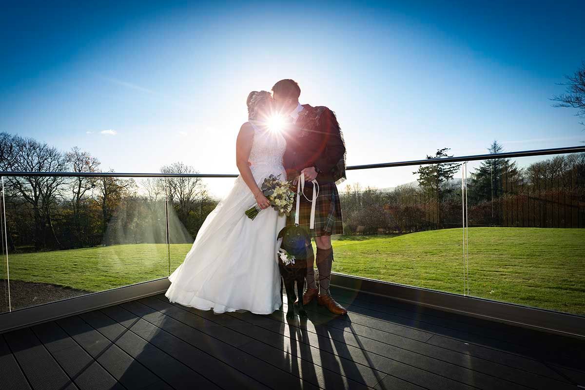 Bride and groom kissing on a sunlit terrace at Hetland Hall for their wedding photographs