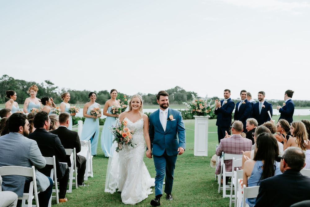 Bride and groom walk down the aisle at an outdoor wedding ceremony on a lush green lawn.