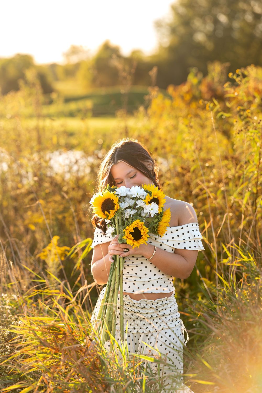 Teen girl holds sunflower bouquet in glowing sunset field during senior portrait session.