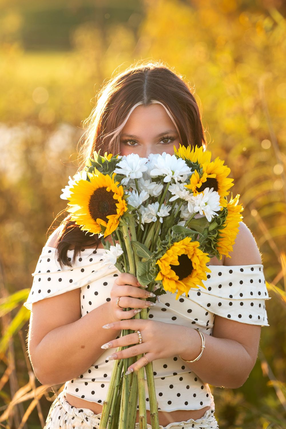 Young woman hiding face behind sunflowers and white daisies bouquet in sunny field.