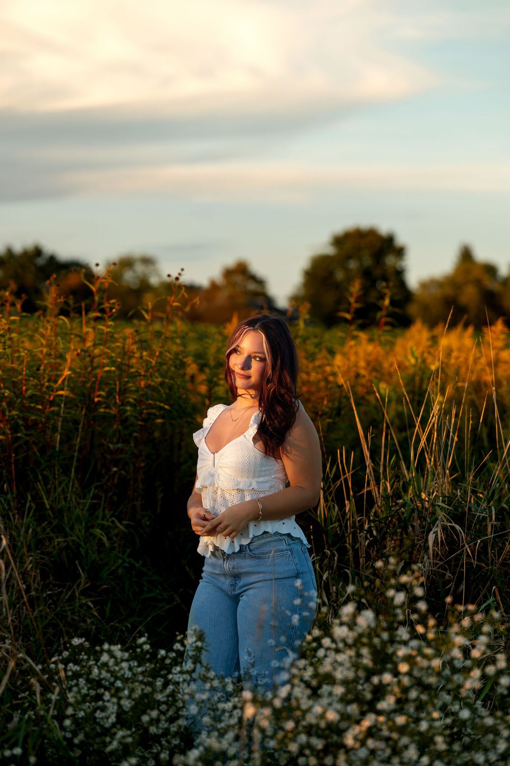 Young woman in white top and jeans poses in golden hour wildflower field.
