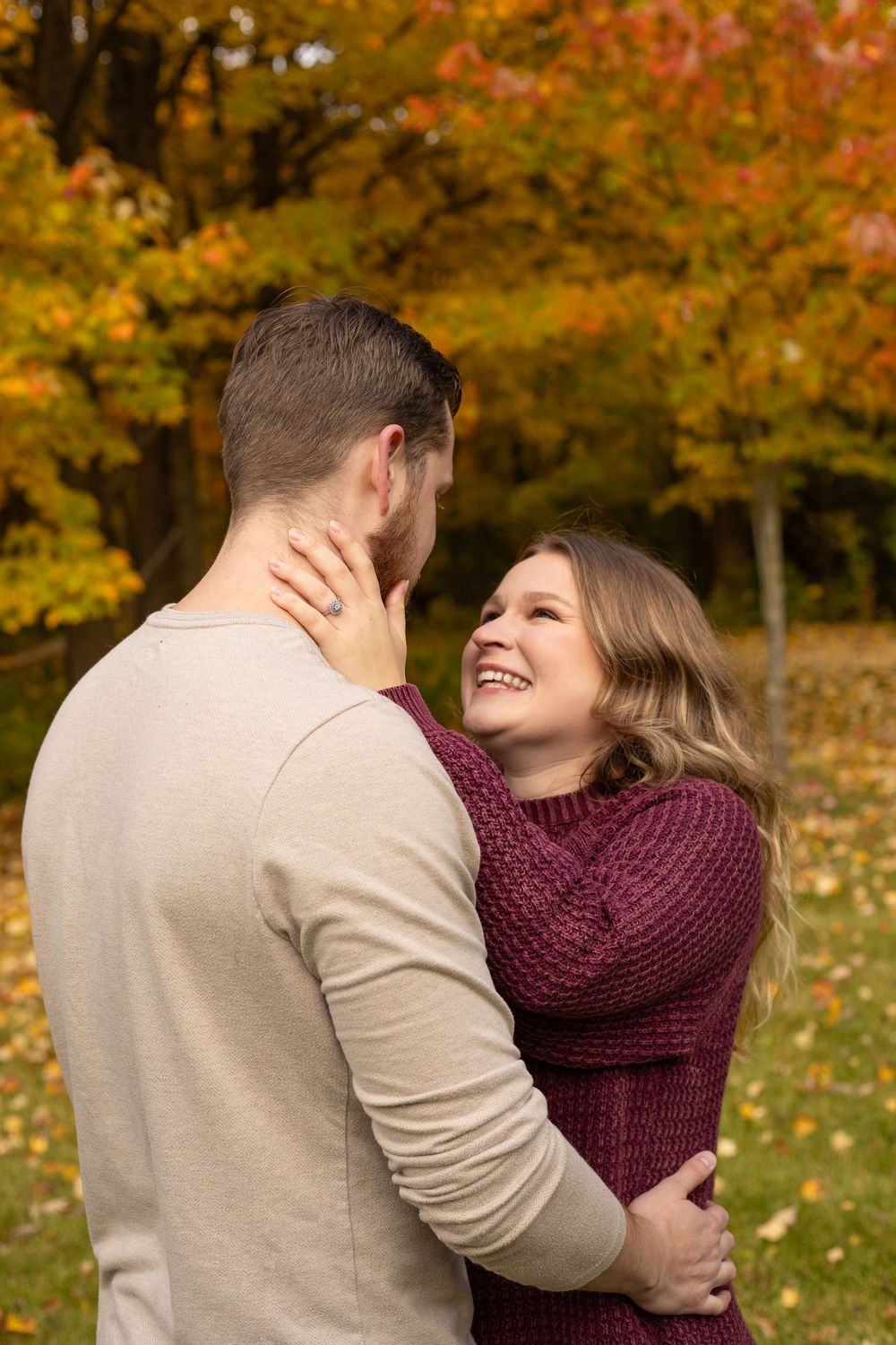 Couple embracing and smiling in autumn park with colorful fall foliage in background.