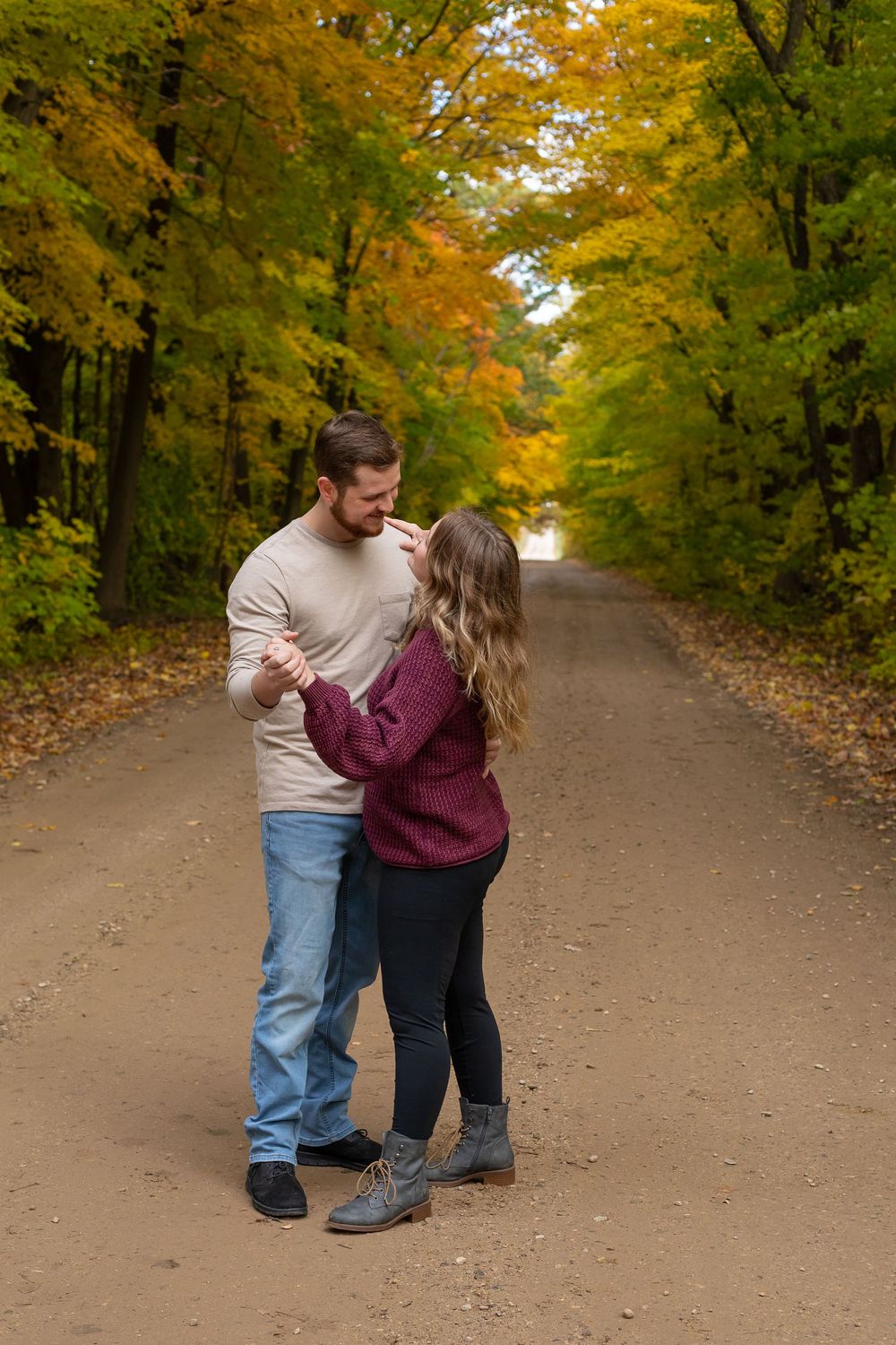 Couple dancing on a scenic dirt road surrounded by colorful autumn foliage in a romantic fall outdoor setting.