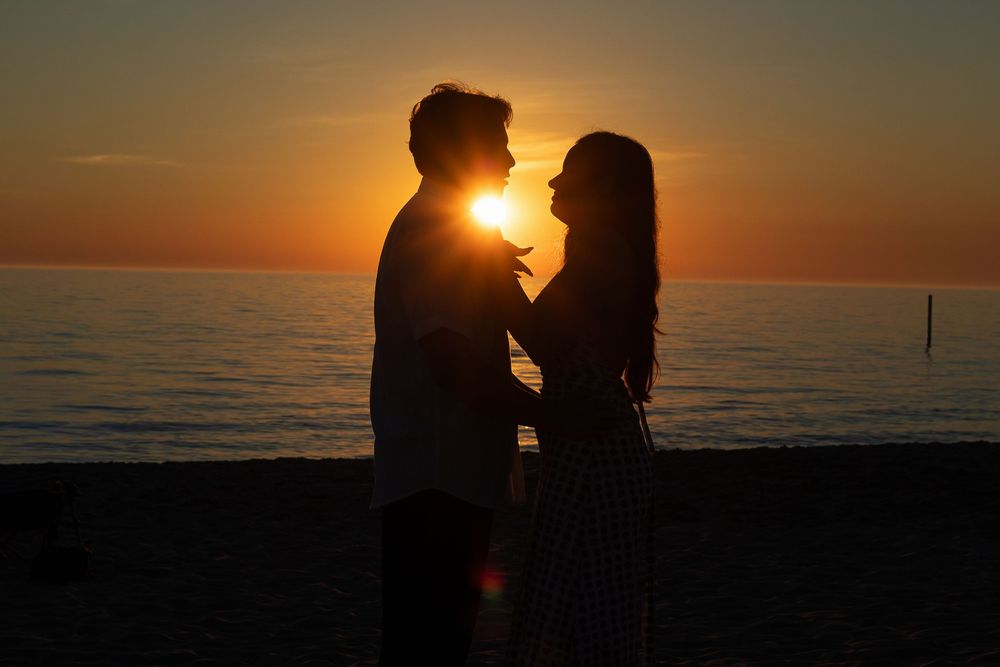 Romantic couple silhouetted against a stunning ocean sunset, sharing an intimate moment on the beach.
