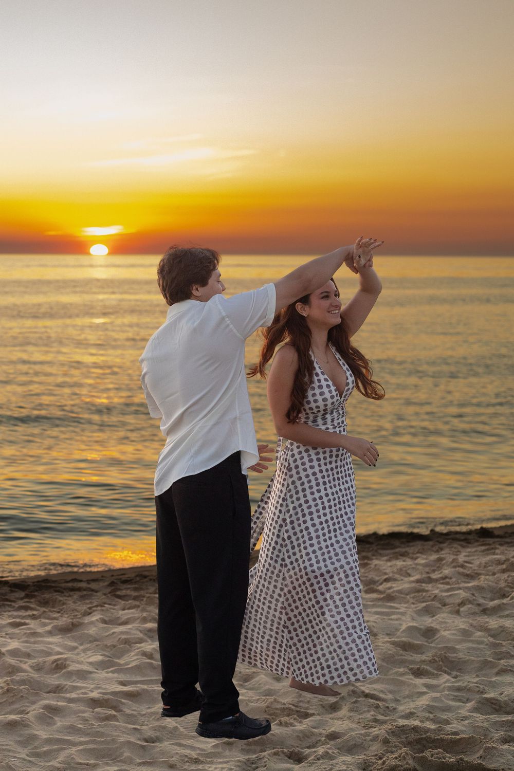 Couple dancing romantically on a sandy beach at sunset with golden ocean backdrop.
