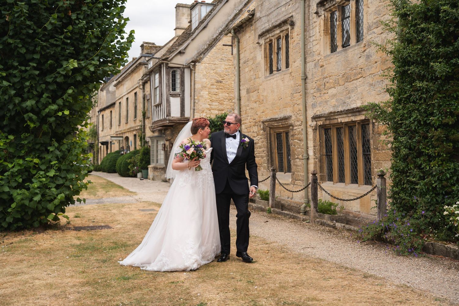 Bride and groom walking together outside a historic stone building on their wedding day.