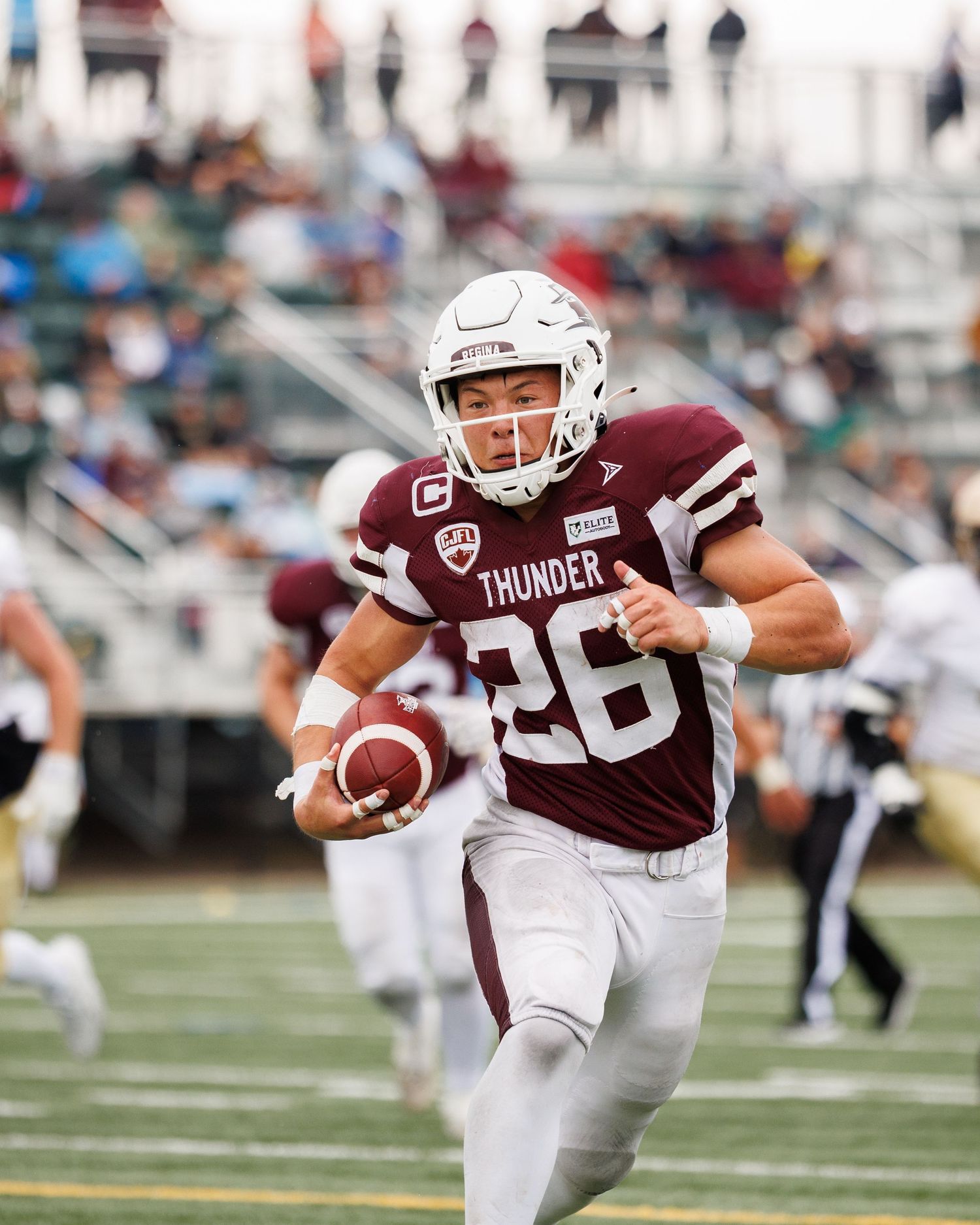 Football player #26 in maroon Thunder uniform runs with ball during game.
