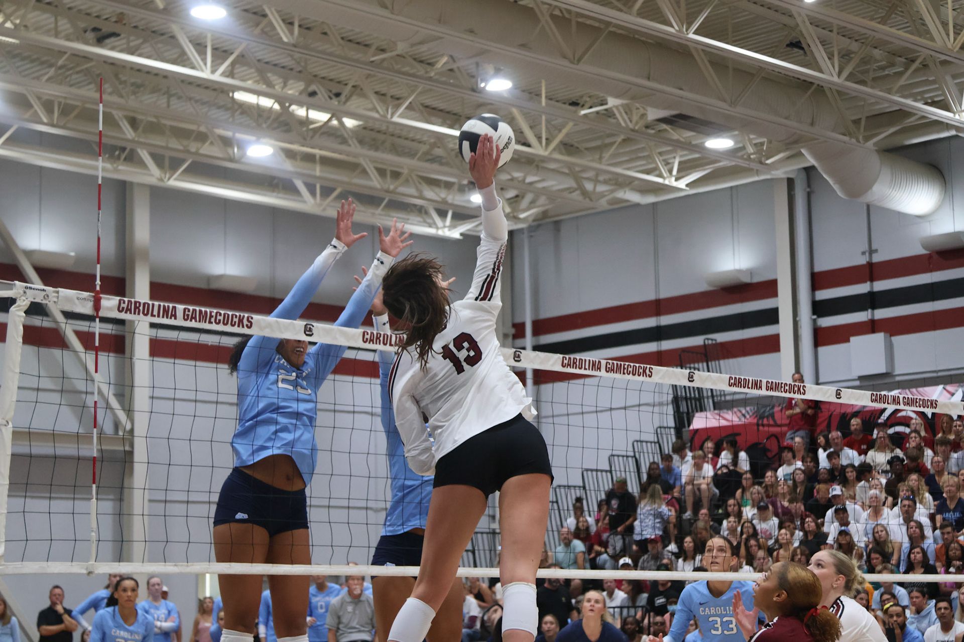 South Carolina volleyball player wearing number 13 attacks the ball over a blocker.