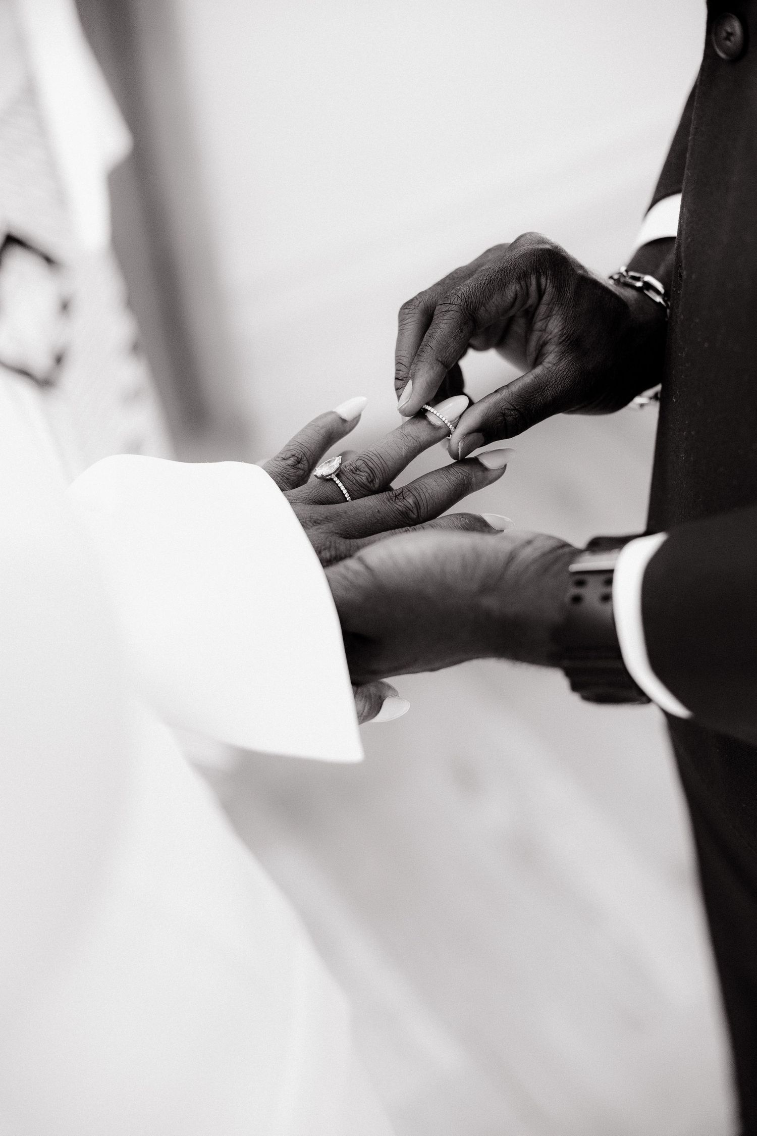 Black and white photo of groom placing wedding ring on bride's finger during ceremony.