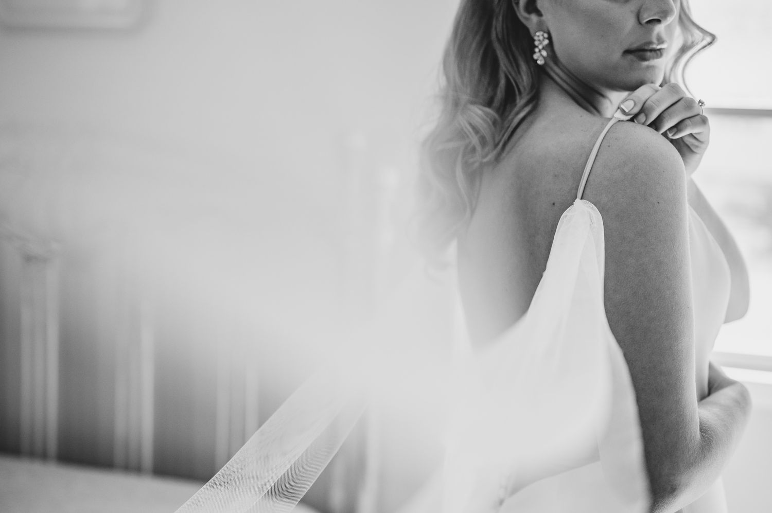 An elegant white wedding dress hangs by a window in a luxurious room with ornate wooden panels and flowing curtains.