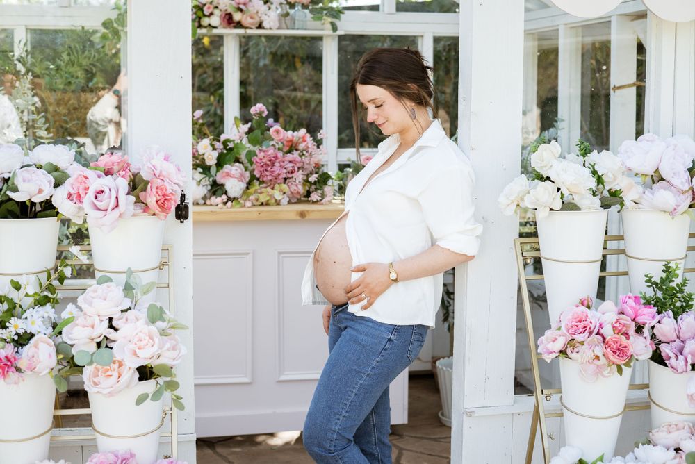 Romantic maternity photos with pink floral decorations in a white greenhouse setting.