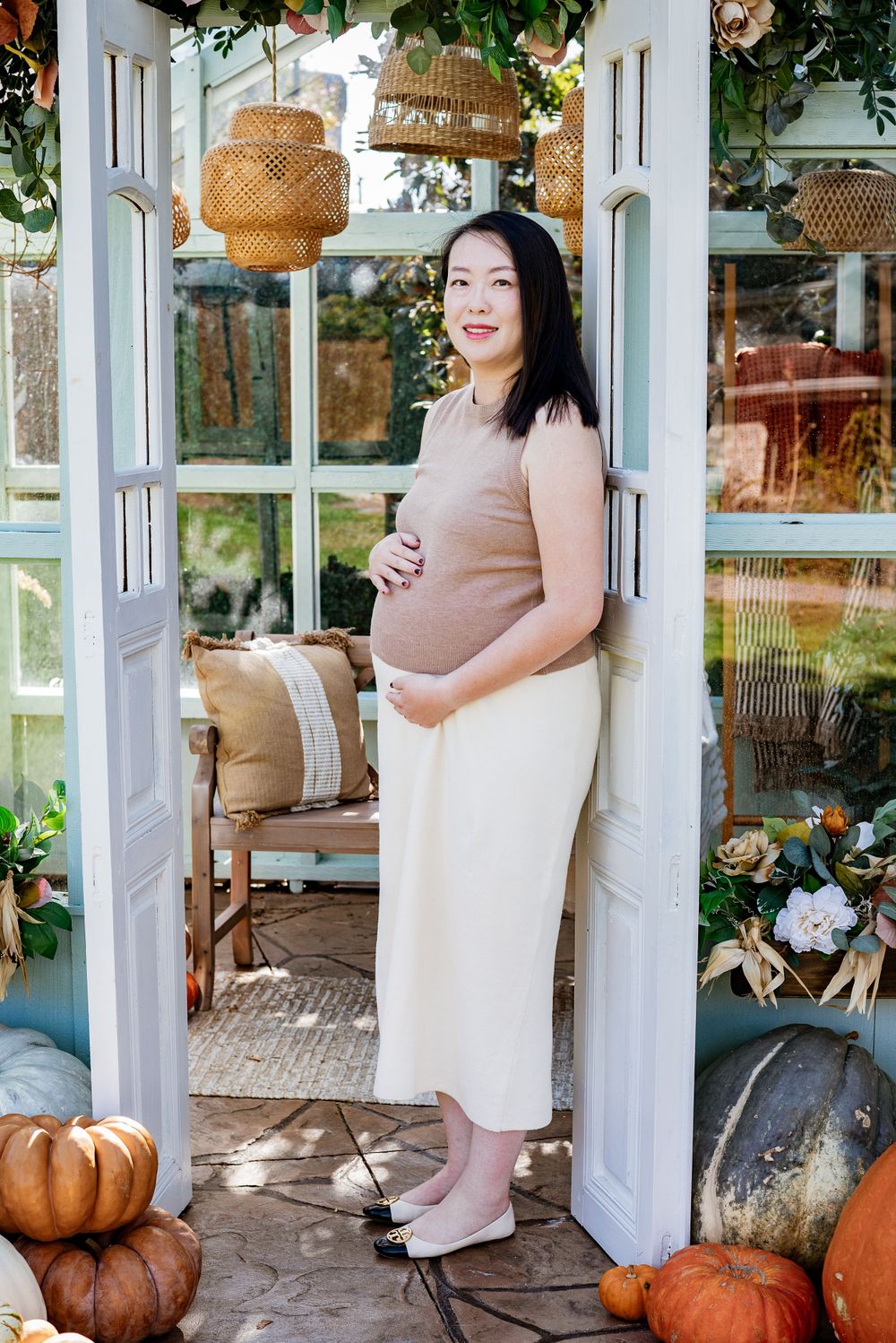Maternity photoshoot in a sunlit greenhouse with pumpkins and autumn decor.