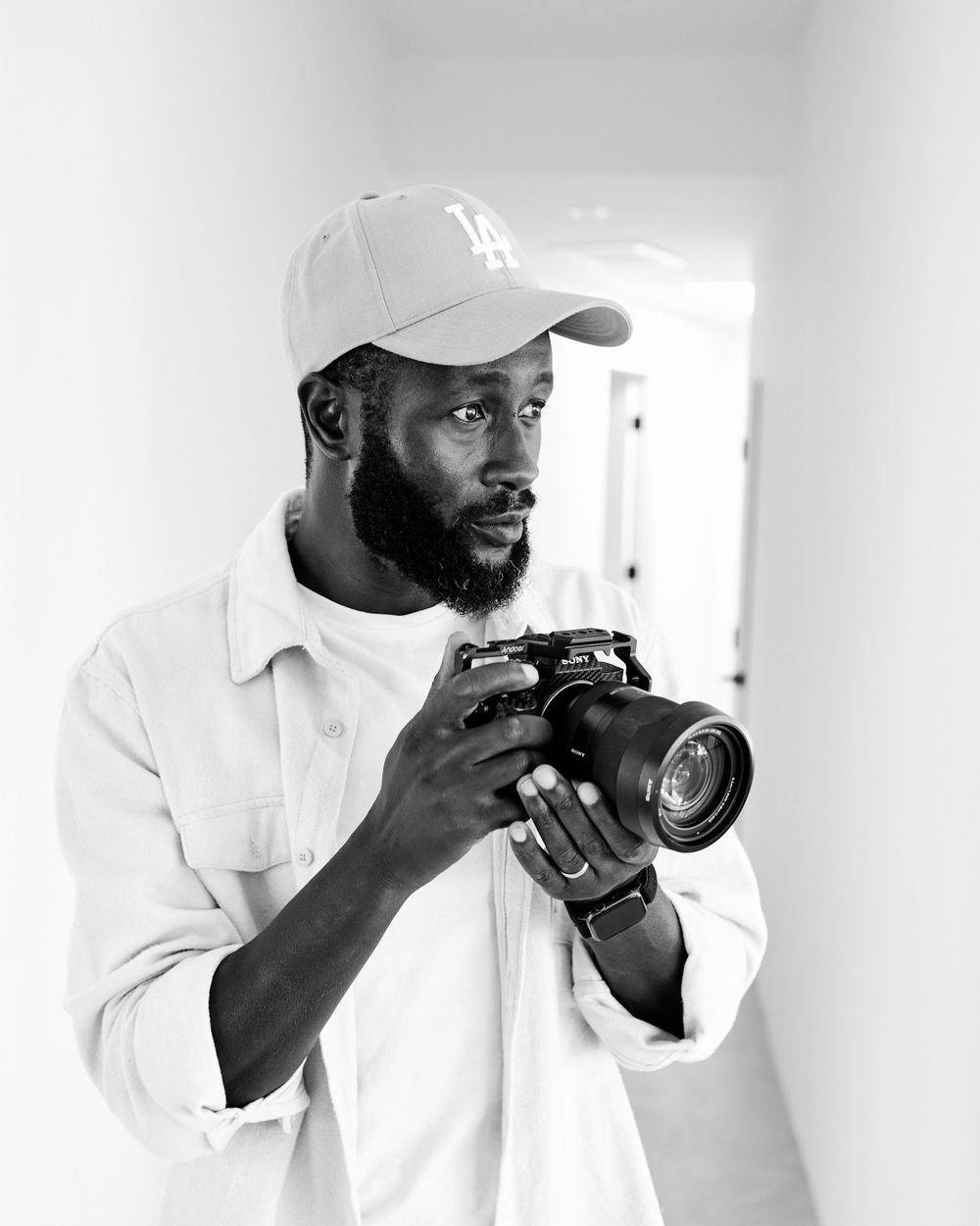 Photographer in white clothes and baseball cap holding camera.