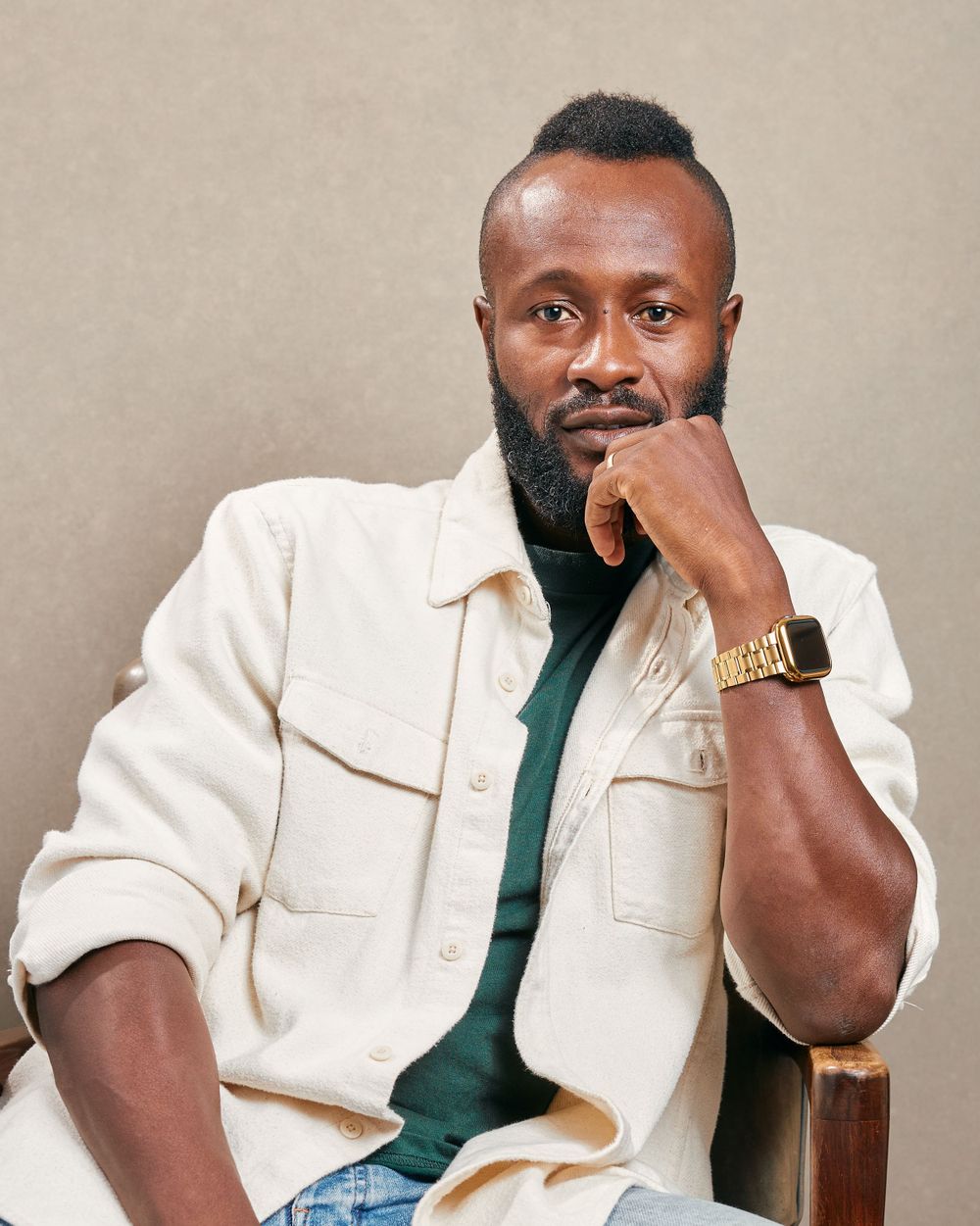 Portrait against beige wall wearing cream jacket and dark green shirt.