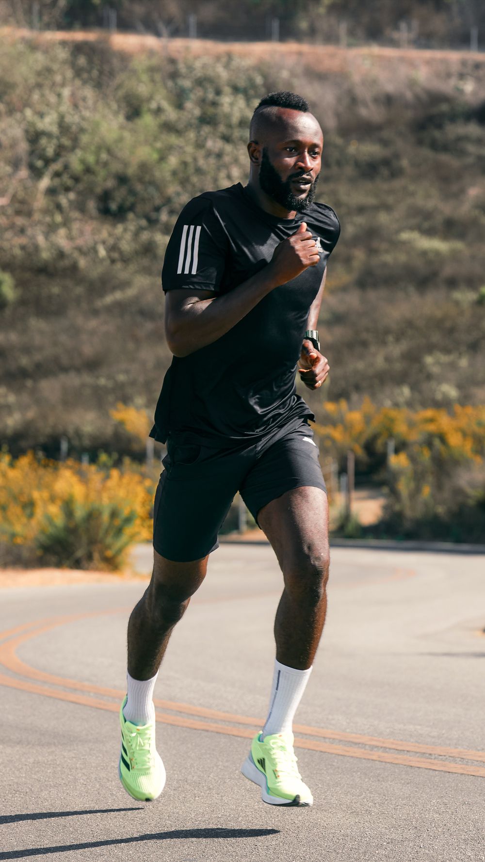 Athlete running on road wearing black activewear and neon green shoes.
